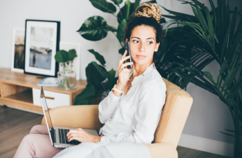 young woman using mobile phone whilst working on a laptop computer