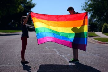 Two people holding a multi coloured rainbow flag