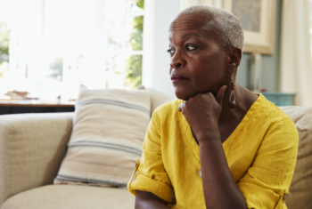 Black older woman sitting down resting chin on hand