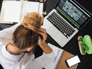 Woman holding her head in her hands over a laptop feeling the effects of being stressed and facing burn out