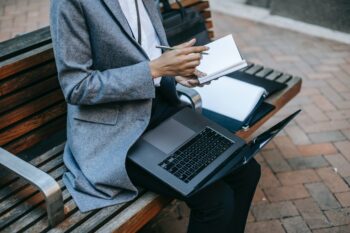 Person depicted sitting on a bench with a notepad and laptop on their knee, Wellbeing while job-hunting during a pandemic